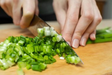 Kadınların elleri, tahta bir tahtada yeşil soğanları bıçakla kesiyor.