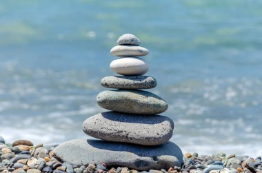 Sahildeki deniz taşları piramidi güneşli bir günde deniz dalgalarının arka planına karşı. Denge ve meditasyon kavramı. Boşluğu kopyala