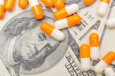 Dolar banknotlarının arka planında bir sürü beyaz ve turuncu tablet var. Sigorta, ilaç, makro