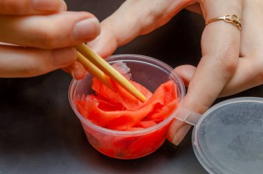 Bir elinde zencefil ve çubuk, diğer elinde de siyah arka planda bir kavanoz.