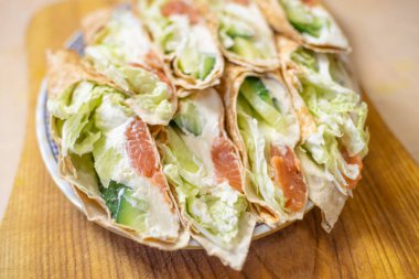 Somon balıklı tortilla rulosu, taze peynir, marul ve tabakta taze salatalık.