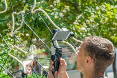 Erkek blogcu, güneşli bir yaz gününde Steadicam videosuyla telefonda çekim yapıyor.