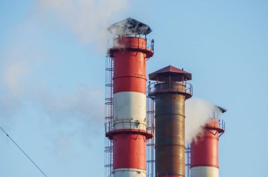 Duman, mavi gökyüzüne karşı üç endüstriyel borudan yayılan emisyon. Uzakta uçak var.