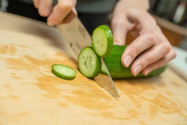 Kadınların elleri taze bir salatalığı ahşap bir tahtanın üzerinde daire şeklinde kesiyor.