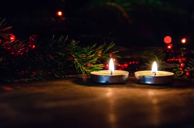 Noel ağacının dalları ve kırmızı boncuklar ve Noel çelenklerinin arkaplanındaki ahşap arka planda iki küçük yuvarlak mum. Güzel Noel arkaplanı, kart