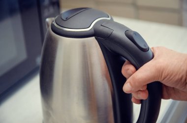 Elektrikli çaydanlık tutan yaşlı bir kadının eli. Yakın plan, kopyalama alanı.