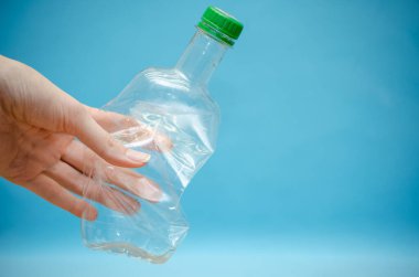 Kadının eli buruşmuş plastik bir şişeyi tutuyor. Üzerinde yeşil bir kapak var. Arka planda da fotokopi alanı var.