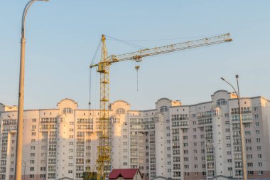 Sarı kule vinci ve açık mavi gökyüzüne karşı çok katlı bir bina.