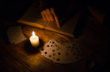 Kartlar, bir kitap, bir mum, ahşap masada bir el. Büyü eğitimi. Kehanet kavramı, sihir.