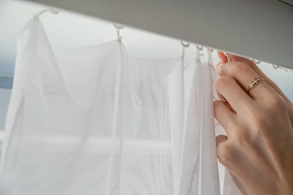 Woman hangs up or removes white curtains indoors, close-up