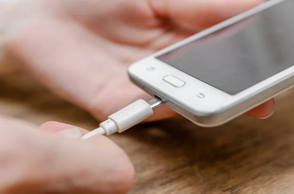 Female hand connecting a white lightning charging cable to a mobile phone - USB data cable to a modern gadget. Close up