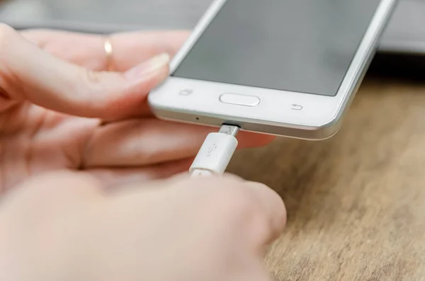 Female hand connecting a white lightning charging cable to a white mobile phone - USB data cable to a modern gadget. Close up