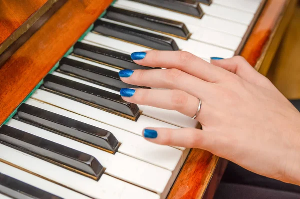 hand of a young woman with blue nail Polish plays the piano close up