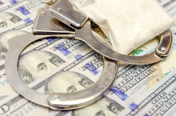 Handcuffs and a bag of drugs close up on dollar bills