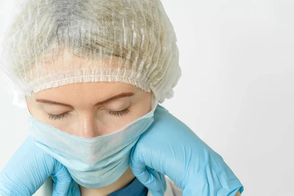 tired woman doctor in a medical mask and medical cap propped her chin in her blue-gloved hands and closed her eyes, copy space