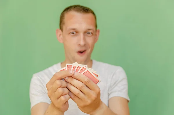 一个绿色背景的男人看着他的卡片 微笑着 扑克中的好卡片 专注于打牌 — 图库照片