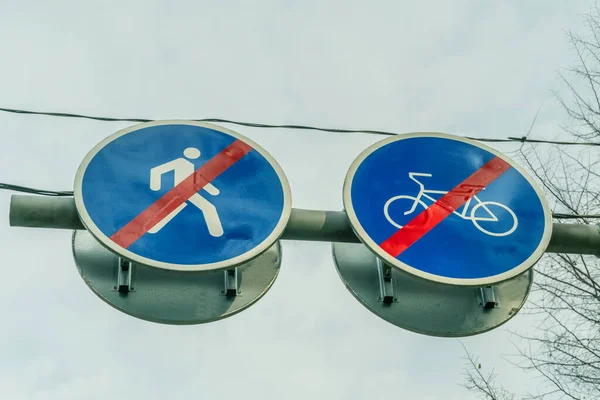 Two road signs side by side for pedestrians and cyclists close up against the sky and tree branches showing that the drive and pass is over