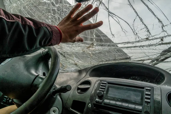 The man hand rests on the broken windshield of the car photo from inside the car