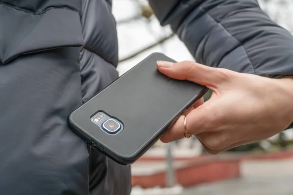 woman\'s hand with a ring pulls a black smartphone out of the pocket of a gray jacket close up