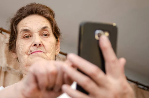 Starsza Kobieta Ciemnymi Włosami Trzyma Przed Sobą Czarny Telefon Komórkowy — Zdjęcie stockowe