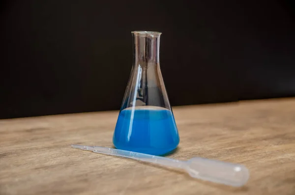 装有蓝色实验室染料的化学瓶在黑色背景上 专门知识和医学的概念 — 图库照片