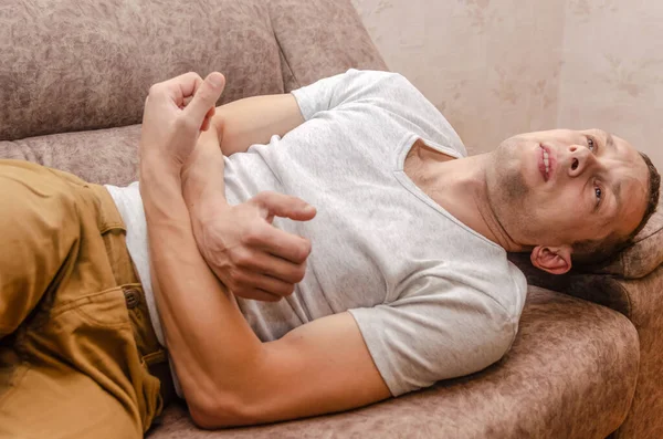 一个穿着棕色裤子和白色T恤的男人躺在沙发上 肚子痛 — 图库照片