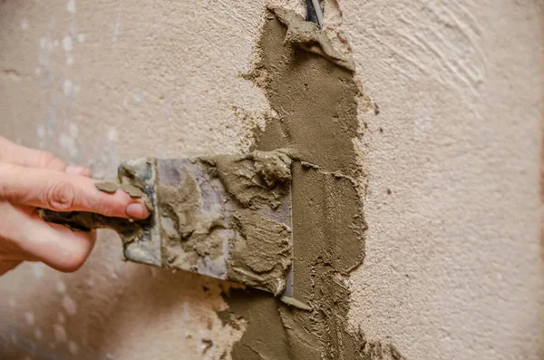 Technical hole in the wall with electrical wiring inside. Master with a spatula and cement mixture closes the hole, safety