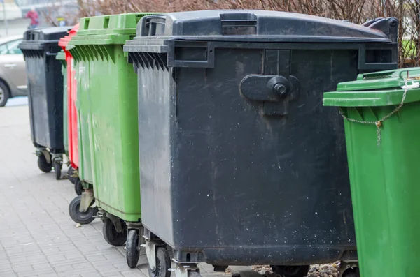 A row of green and black garbage cans along the street.