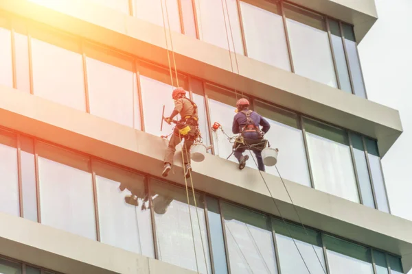 Two workers are washing the windows of a high-rise glass building. Work at heights, industrial mountaineering. Photos with flare — Stock Image Two Workers Washing Windows High Rise Glass Building Work Heights Stock Picture