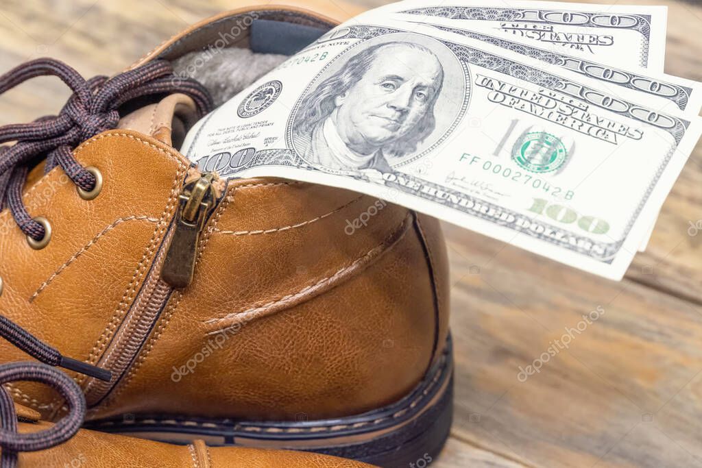 Concept photo of brown leather men's shoes, with dollars inside the shoes on a wooden background