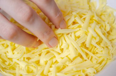 Kadının eli parmaklarıyla tabaktan rendelenmiş büyük bir peynir alıyor..