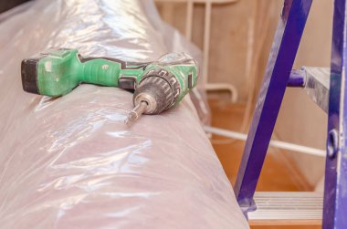 Işık yüzeyindeki elektrikli tornavidayı kapat, yanında bir merdiven var. İnşaat, onarım ve bakım konsepti.