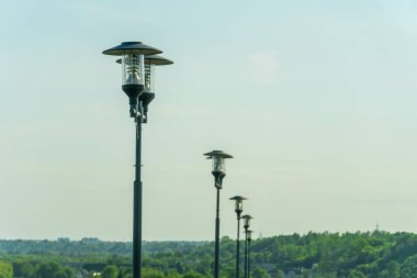 Açık mavi bir gökyüzünün arka planında sisli ve yeşil ağaçlı sokak ışıkları