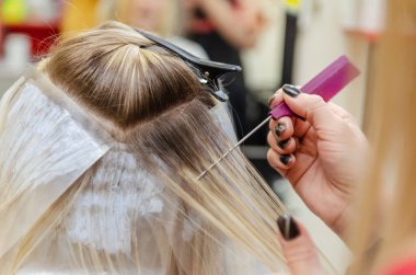 Kuaför saç boyamak için saç tellerini dağıtır.