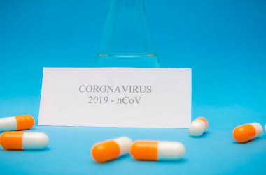 Temiz bir sıvı, turuncu-beyaz kapsüller, mavi arka planda Coronavirus yazısıyla beyaz bir sayfa.