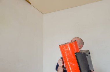 İşçi bir ısı tabancası tutuyor ve tavana doğrultuyor. Gerilme tavanı kurulumu. Boşluğu kopyala