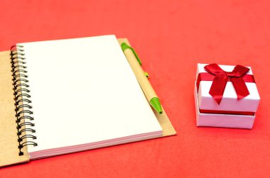 Kırmızı arka planda kalem ve hediye ile Notepad 'i aç. Tatil konsepti, Sevgililer Günü, Noel, Yeni Yıl