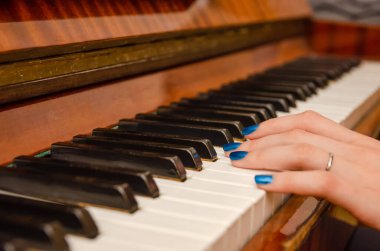 Mavi tırnak cilası olan genç bir kadının eli piyano çalıyor.