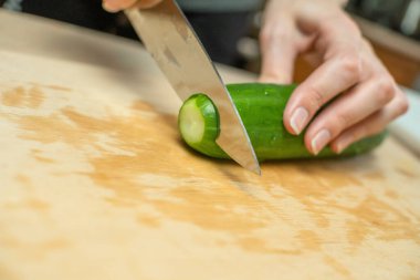 Kadınların elleri taze bir salatalığı ahşap bir tahtanın üzerinde daire şeklinde kesiyor.