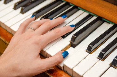 Mavi tırnak cilası olan genç bir kadının eli piyano çalıyor.