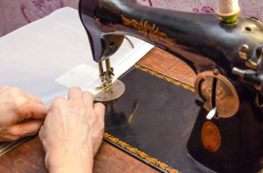 Eski bir dikiş makinesine dikiş diken bir kadının elleri.