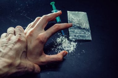 Elinde uyuşturucu paketiyle bir uyuşturucu bağımlısının elini tutuyor. Siyah arka planda bir şırınga. Rehabilitasyon merkezinde rehabilitasyon yoluyla uyuşturucu bağımlılığını durdurabilirsiniz..