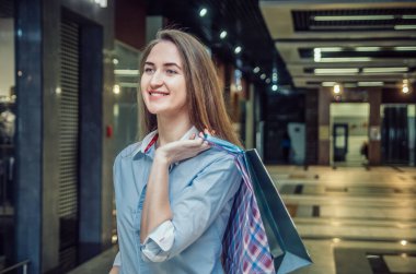 Güzel, kahverengi saçlı, uzun saçlı, alışveriş merkezinde omuzunda bir sürü paket olan bir kız. Neşeli, mutlu alışveriş kızı