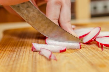 Dişi eller, tahta bir tahtanın üzerinde turpu küçük parçalara ayırıyor.