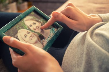 Kızın elleri bir fotoğraf çerçevesi tutuyor. Üzerinde iki kızın fotoğrafı var. Sarışın, kahverengi saçlı, yakın çekim, sıcak fotoğraf.