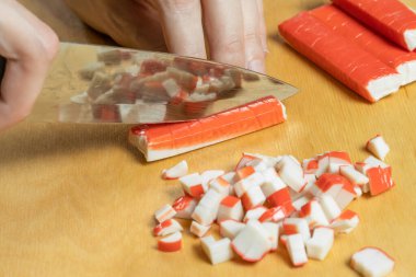 Kadın eli, tahta bir tahtada yengeç sopası keser. Yaklaş.