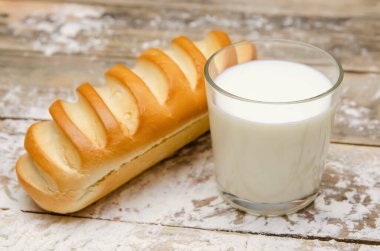 Bir bardak süt ve ahşap zemin üzerinde küçük bir somun un.