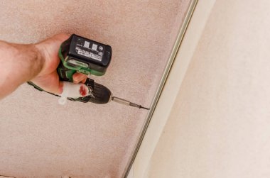 Adamın elleri tavandaki metal çerçeveyi elektrikli tornavidayla onarıyor. Onarım, inşaat, DIY konsepti.