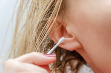 Sarışın kadın kulağını beyaz pamuklu çubukla temizliyor.