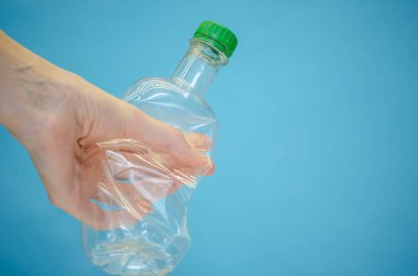 Kadının eli buruşmuş plastik bir şişeyi tutuyor. Üzerinde yeşil bir kapak var. Arka planda da fotokopi alanı var.